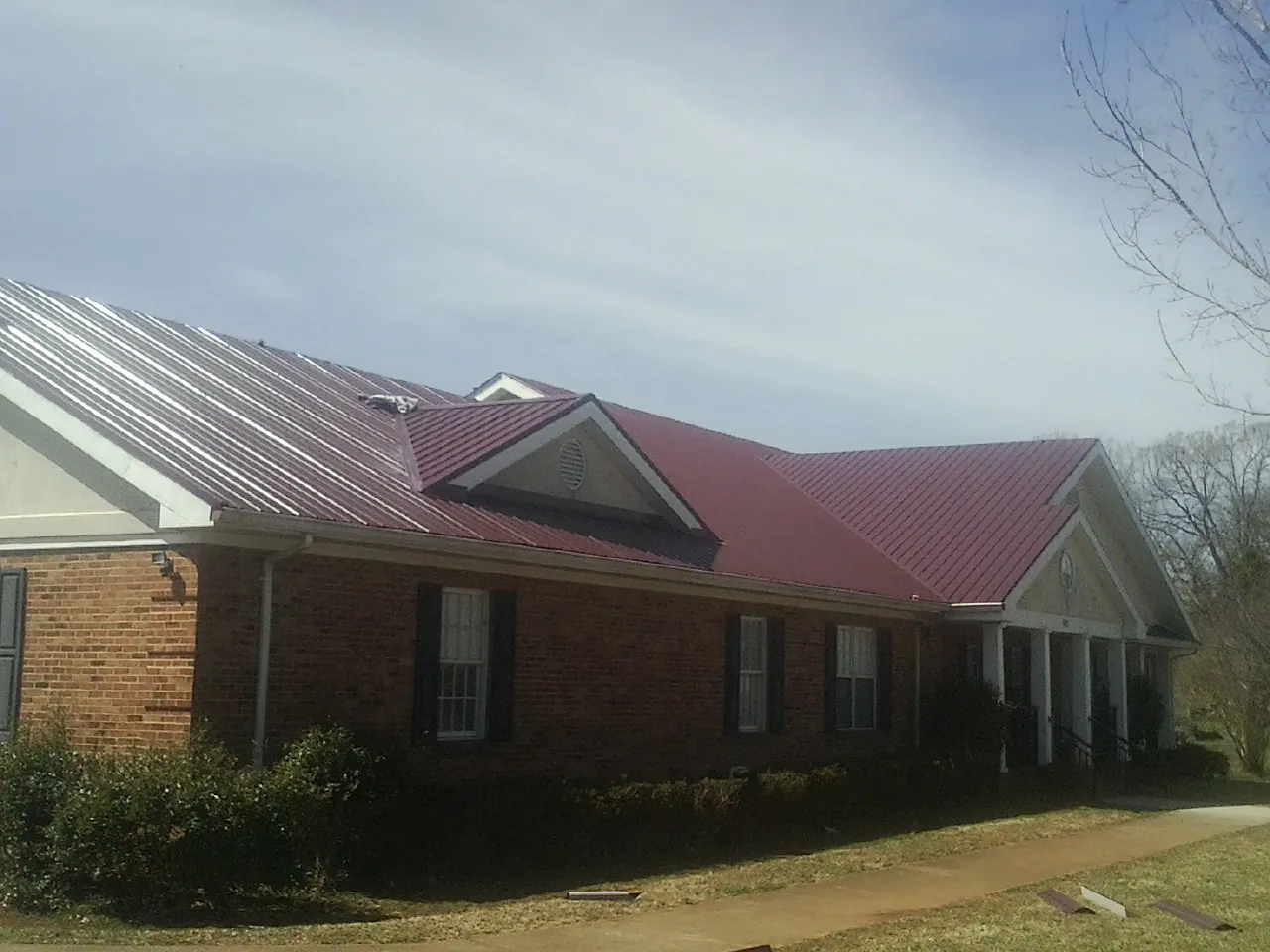 Red metal roof with gabled entries on a long brick building, from a Hail Damage Roof Repair job in Hales Corners