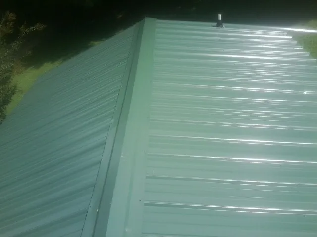 New green metal panels meeting at the ridge of a roof — Flat Roof Repair work by our crew in Hales Corners