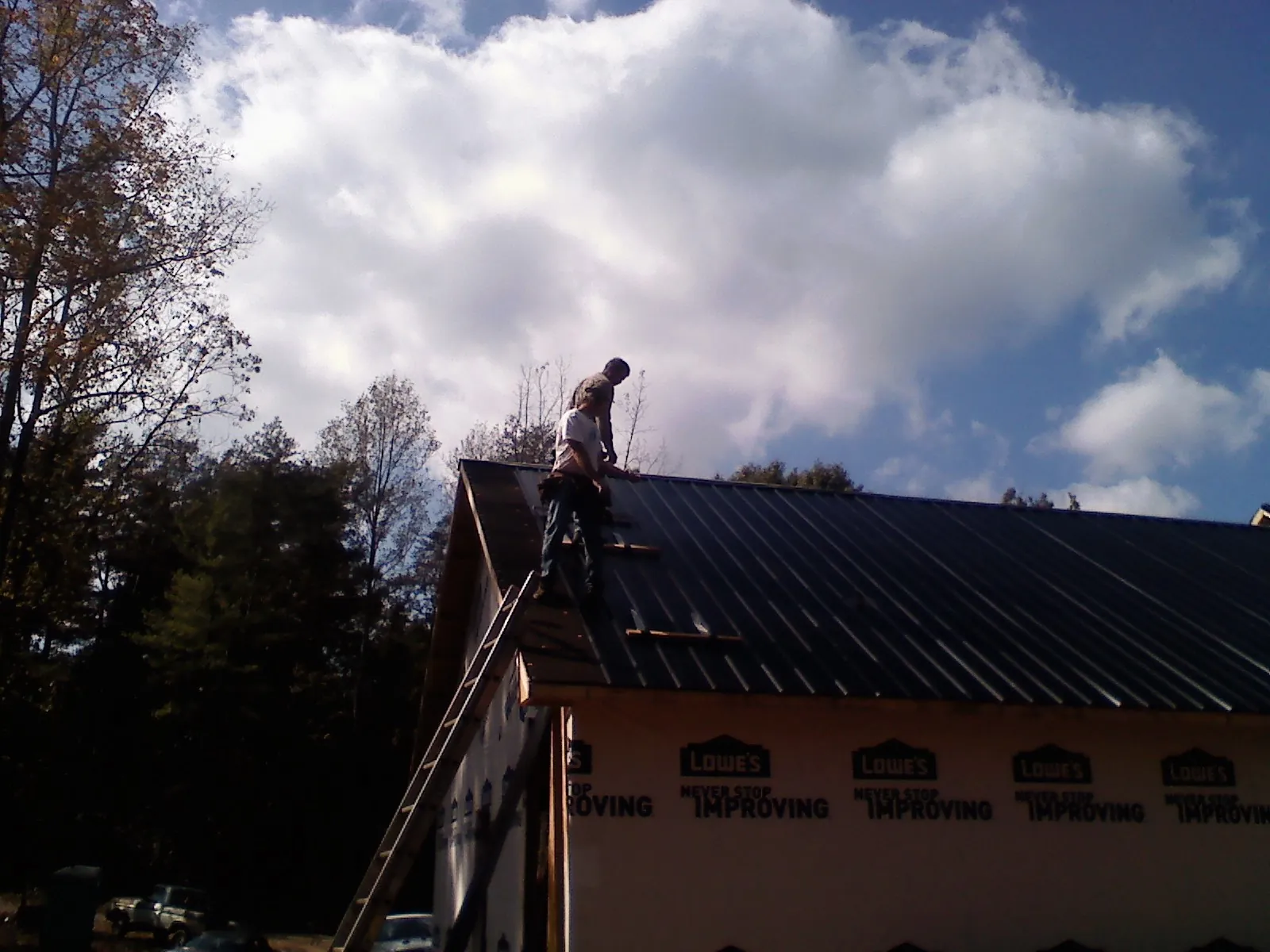 Roofer fastening dark metal panels high against a cloudy sky, from a Roof Inspection job in Hales Corners