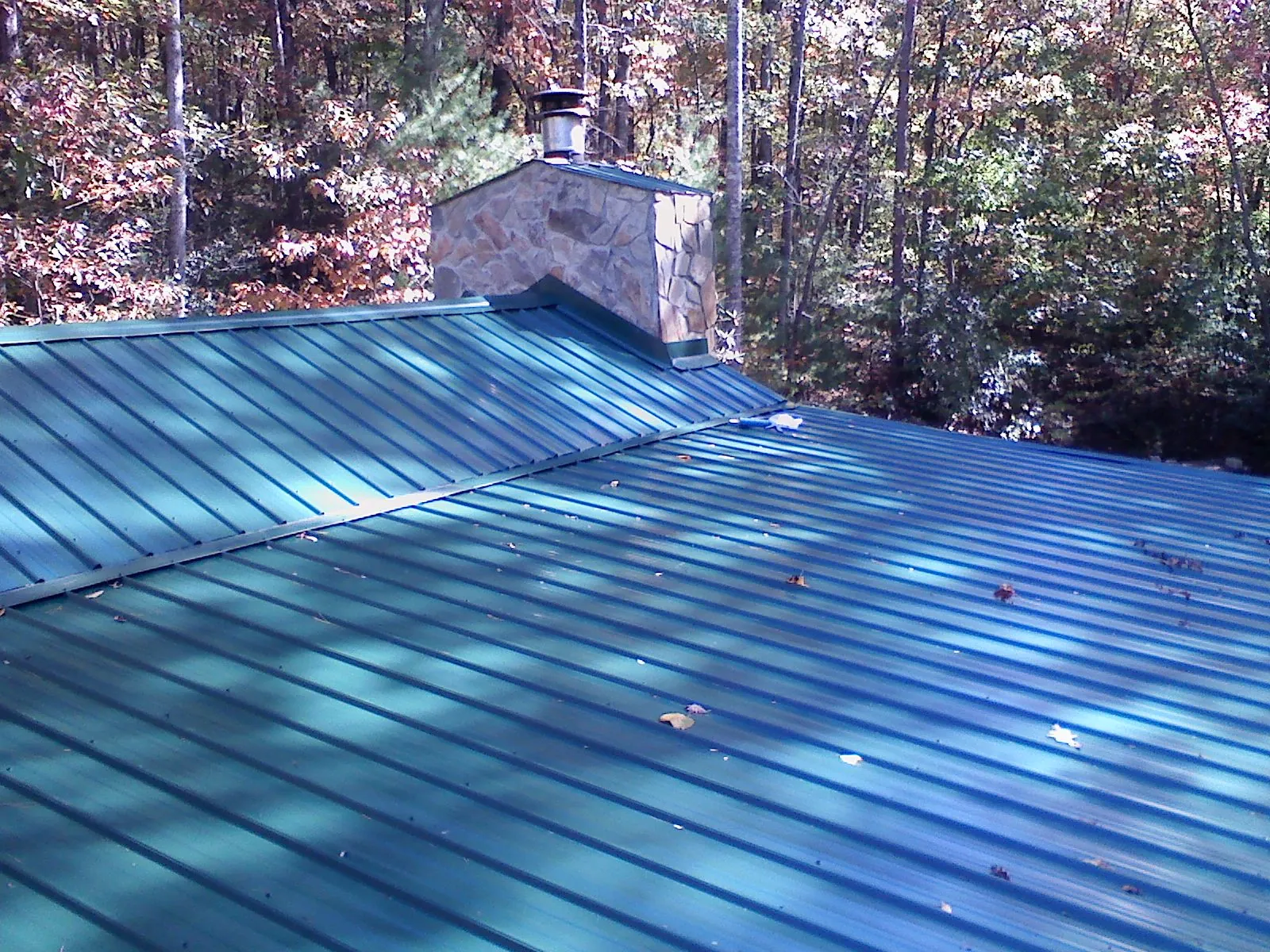 New green metal roof and stone chimney surrounded by autumn woods in Hales Corners