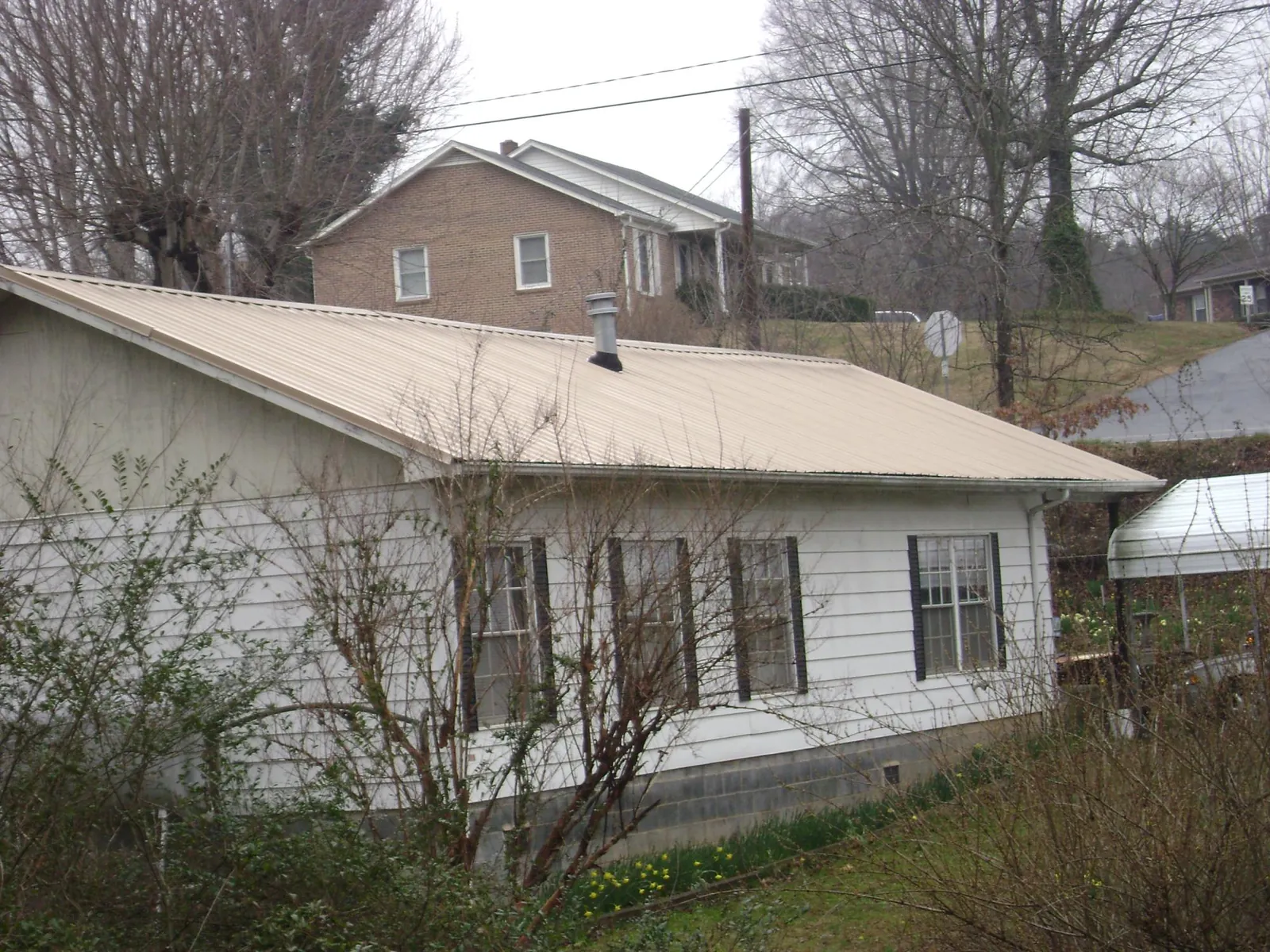 Tan metal roof on a white sided house set into a hillside — Commercial Roofing by Roofing Brothers in Hales Corners