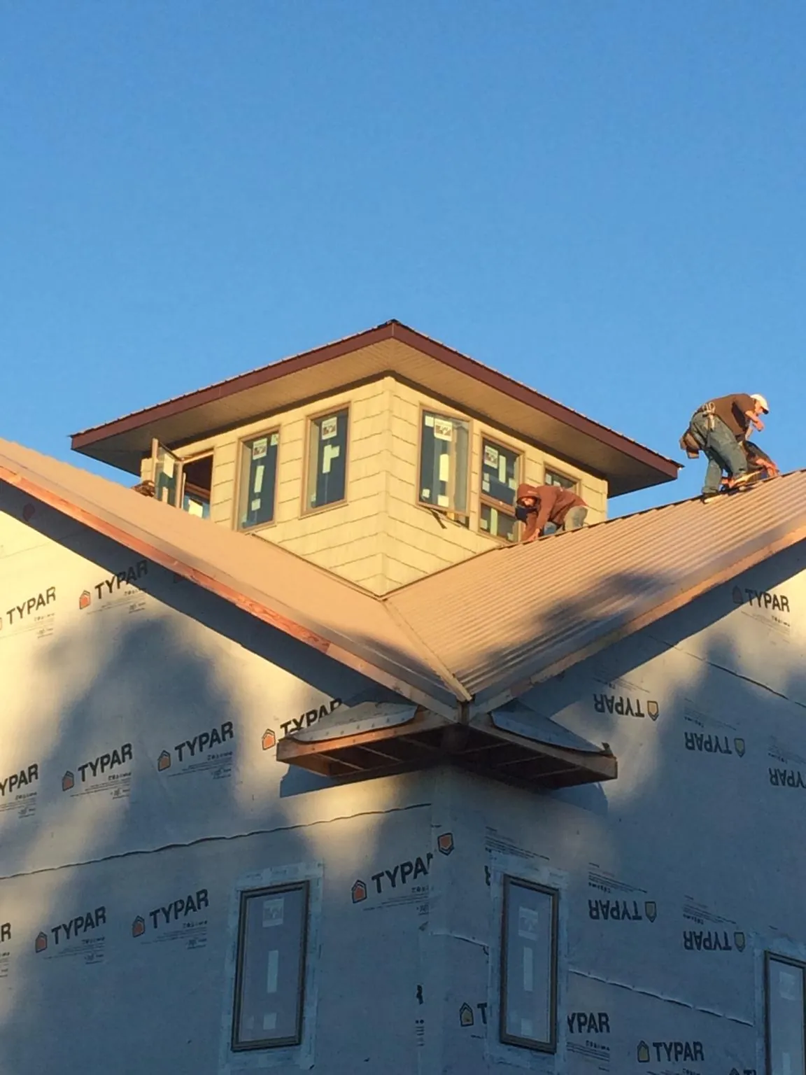 Roofers working around a rooftop cupola on a new metal roof at sunset — Roof Waterproofing in Hales Corners by Roofing Brothers